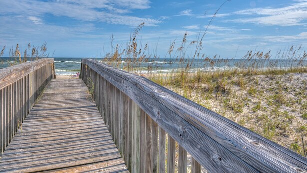 A wooden boardwalk leading to a beach with sand dunes and sparse vegetation.