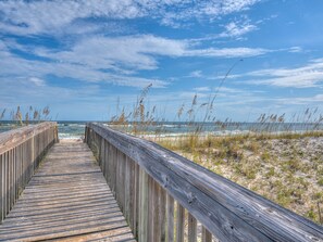 Ein hölzerner Gehweg führt zu einem Strand mit Dünen und vereinzelter Vegetation.