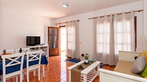 A living room with a television, white furniture, a wooden door, and large windows with curtains. - Apartment Lima Center Playa Blanca By PVL (playa blanca)