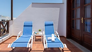 A rooftop terrace with two sun loungers, a small table with a book and a plant, and a wooden door. - Apartment Lima Center Playa Blanca By PVL (playa blanca)