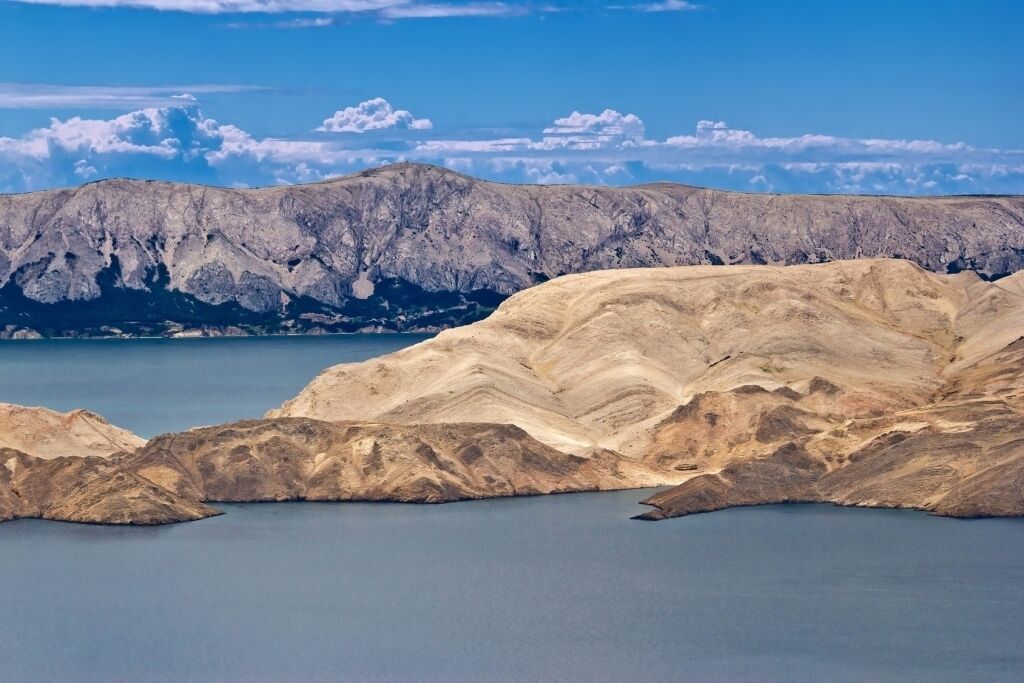 A coastal landscape with a large body of water, rocky terrain, and distant mountains under a clear sky.