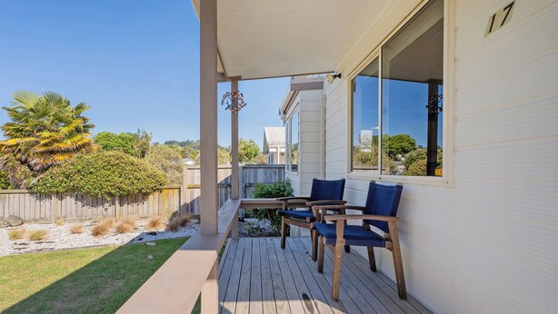 A covered patio with a wooden deck, two blue cushioned chairs, and a small table.