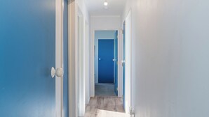A hallway with blue doors, white walls, and a wooden floor. - Nest by the Beach - Cooks Beach Holiday Home (Cooks Beach)
