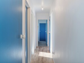 A hallway with blue doors, white walls, and a wooden floor. - Nest by the Beach - Cooks Beach Holiday Home (Cooks Beach)