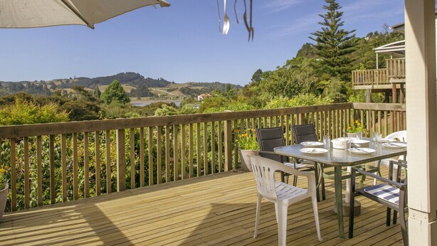 Une terrasse en bois avec une table et des chaises, offrant une vue panoramique sur un paysage vallonné et un plan d’eau.