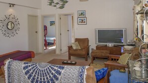 Un salon confortable avec une télévision, un coin salon et une vue sur la mer, visible à travers une porte ouverte.