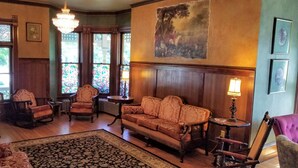 A traditional room with wooden paneling, a sofa, armchairs, a patterned rug, and stained glass windows. - Historic Victorian Inn (Sioux Falls)