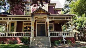 A two-story house with a front porch, a central entrance, and a small garden area. - Historic Victorian Inn (Sioux Falls)