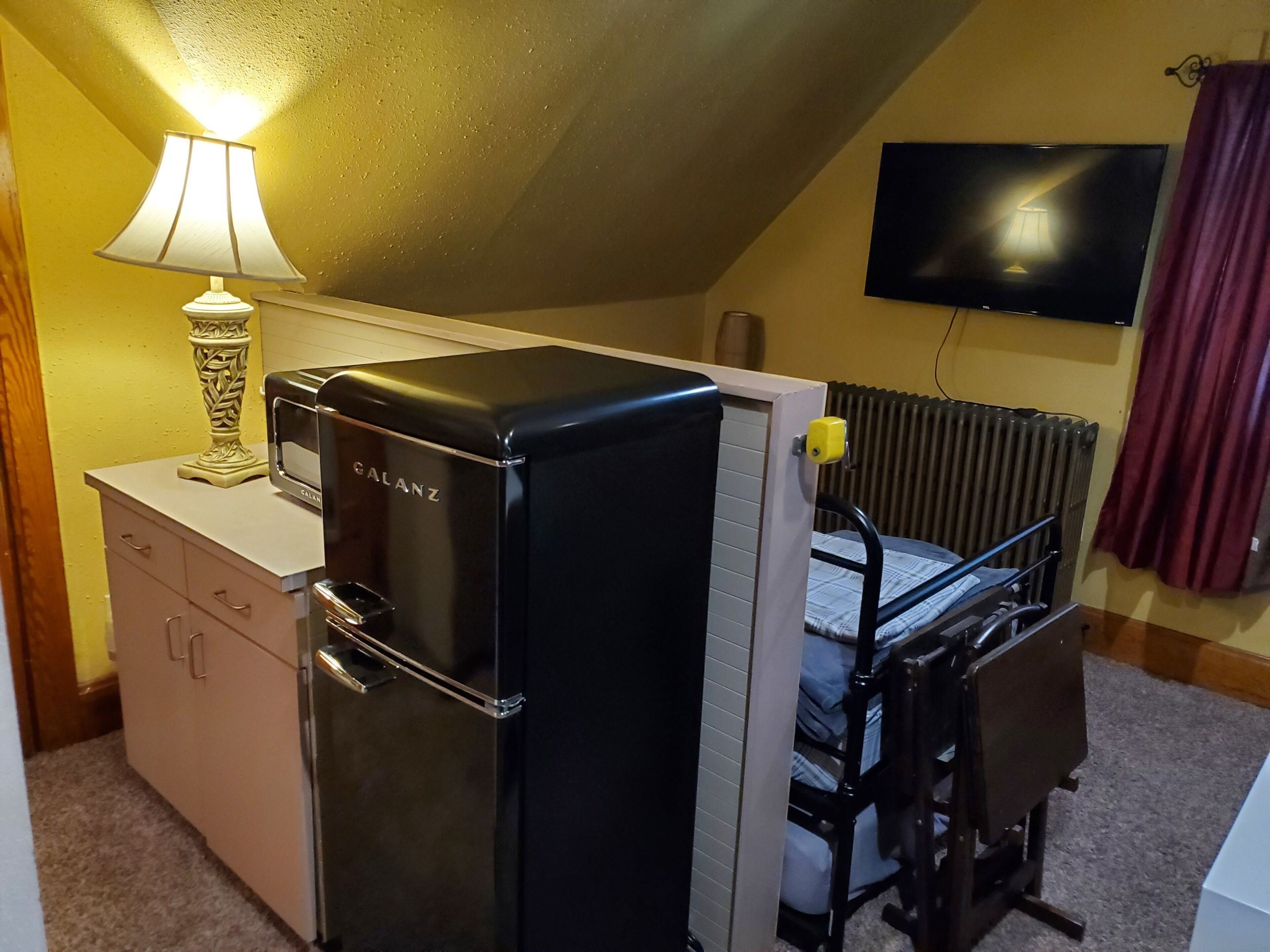 Una habitación pequeña con kitchenette, cama, televisión y radiador.