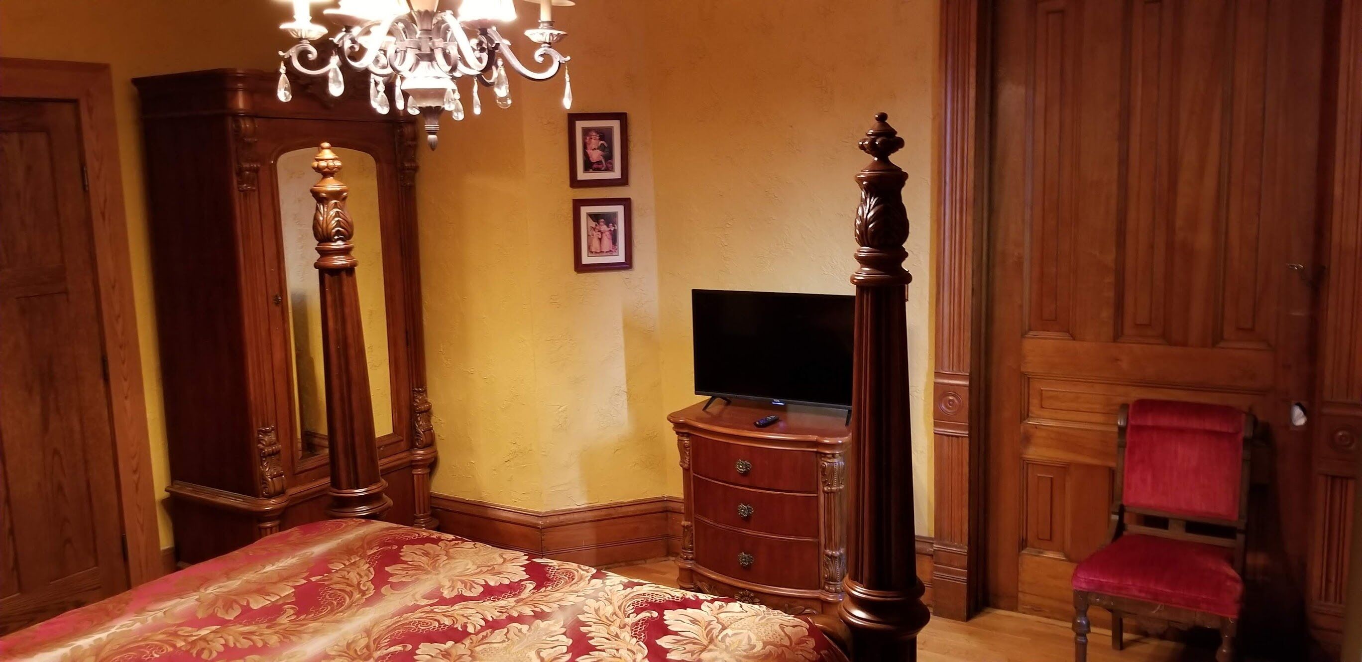 A bedroom with a large bed, a dresser, a television, a chair, and a mirror.