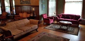 A traditional living room with a brown sofa, a red armchair, and a matching red sofa. There are two side tables with lamps and a coffee table in the center.