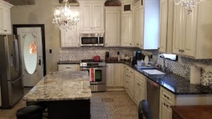 A kitchen with white cabinets, granite countertops, stainless steel appliances, and a chandelier. - Historic Victorian Inn (Sioux Falls)