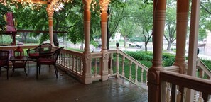 A covered outdoor area with a wooden railing, chairs, and tables. - Historic Victorian Inn (Sioux Falls)