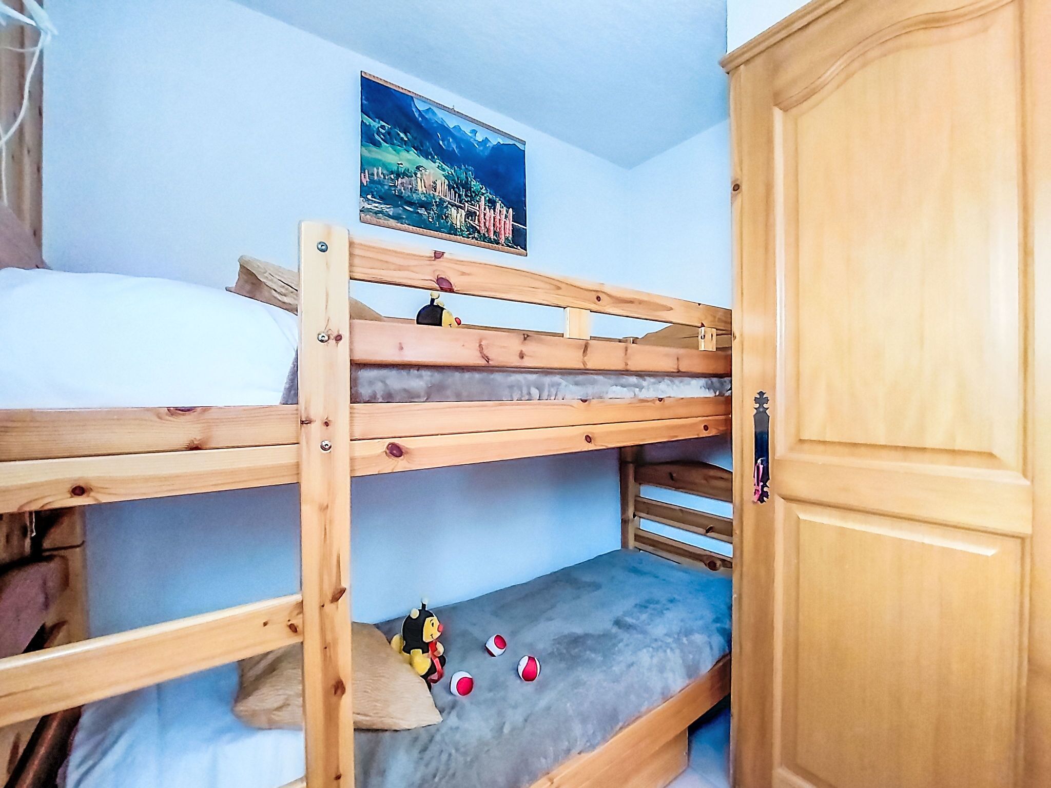 A bunk bed room with a wooden wardrobe and a framed picture on the wall.