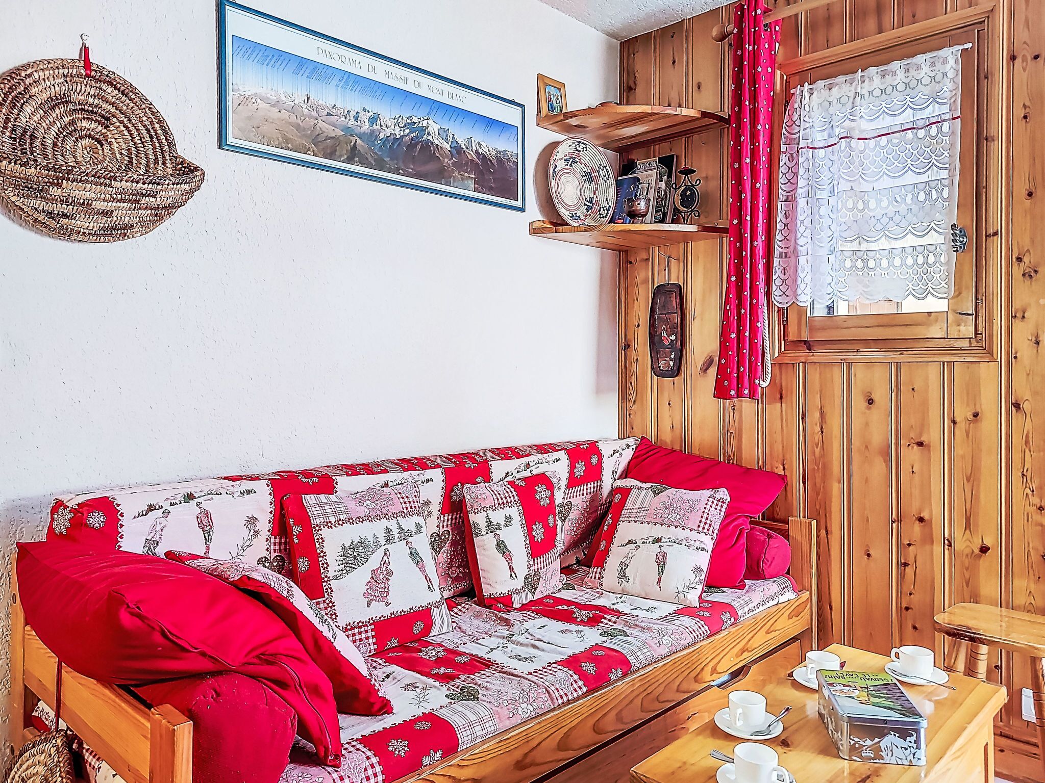 Ein Holzsofa mit gemusterten Kissen, ein Wandbild und ein kleiner Tisch mit Tassen und einer Blechdose.