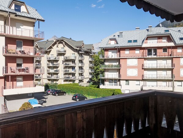 A multi-story residential building with balconies, a parking area, and a clear view of a mountain in the background.