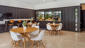 A modern conference room with round tables and white chairs, equipped with a flat-screen TV and a coffee machine. - Downtown Printer Row district Hotel style room (Chicago)