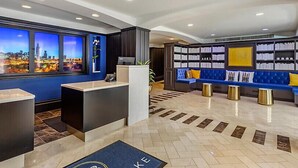 A hotel reception area with a cityscape view, a reception desk, a seating area with bookshelves, and a blue sofa. - Downtown Printer Row district Hotel style room (Chicago)