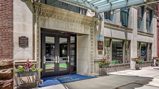 A hotel entrance with a classic facade, a blue carpet, and a sign indicating the address. - Downtown Printer Row district Hotel style room (Chicago)
