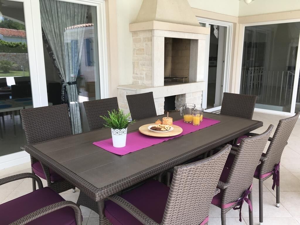 An outdoor dining area with a stone fireplace, wicker chairs, and a table set with food and drinks.