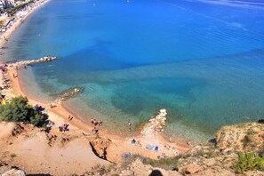 Une plage côtière aux eaux bleues et limpides, bordée de sable et ponctuée de formations rocheuses.