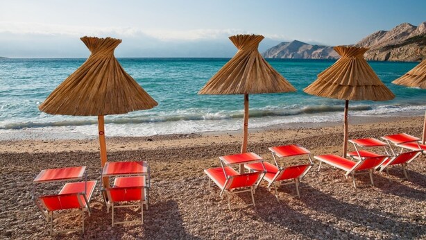 Une plage avec des parasols en chaume et des chaises longues rouges.
