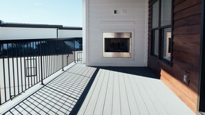 A balcony with a wooden deck, a fireplace, and a view of the sky.