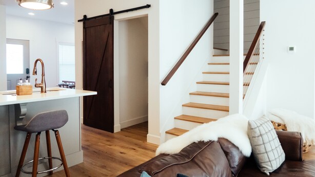 A modern interior with a kitchen area, a staircase, and a seating area with a brown leather couch.