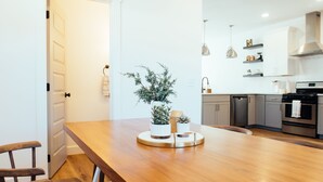 A modern kitchen with a wooden dining table, white cabinets, and pendant lighting.