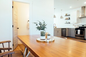 Una cocina moderna con una mesa de comedor de madera, armarios blancos e iluminación colgante.