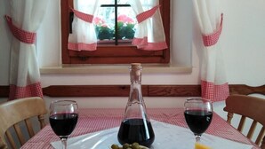 Una mesa de comedor con mantel a cuadros, una botella de vino, copas, una tabla de madera con queso, aceitunas y embutidos.