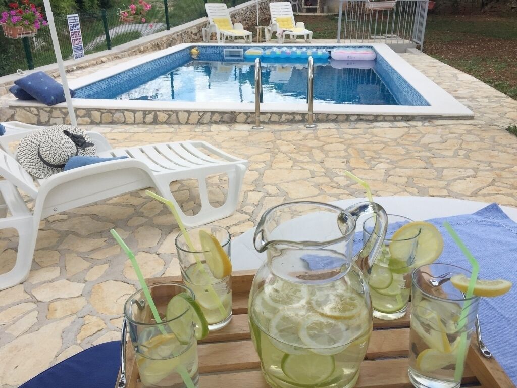 Escena junto a la piscina con un patio de piedra, sillas de descanso y una jarra de limonada con rodajas de limón.