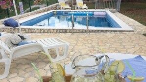Escena junto a la piscina con un patio de piedra, sillas de descanso y una jarra de limonada con rodajas de limón.