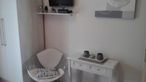 Een moderne kamer met een witte stoel, een klein tafeltje met decoratieve spullen, een wandtelevisie en een kunstwerk aan de muur.