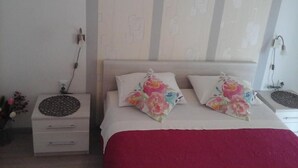Een slaapkamer met een bed, twee kussens, een nachtkastje, een lamp en een muur met een geometrisch patroon.