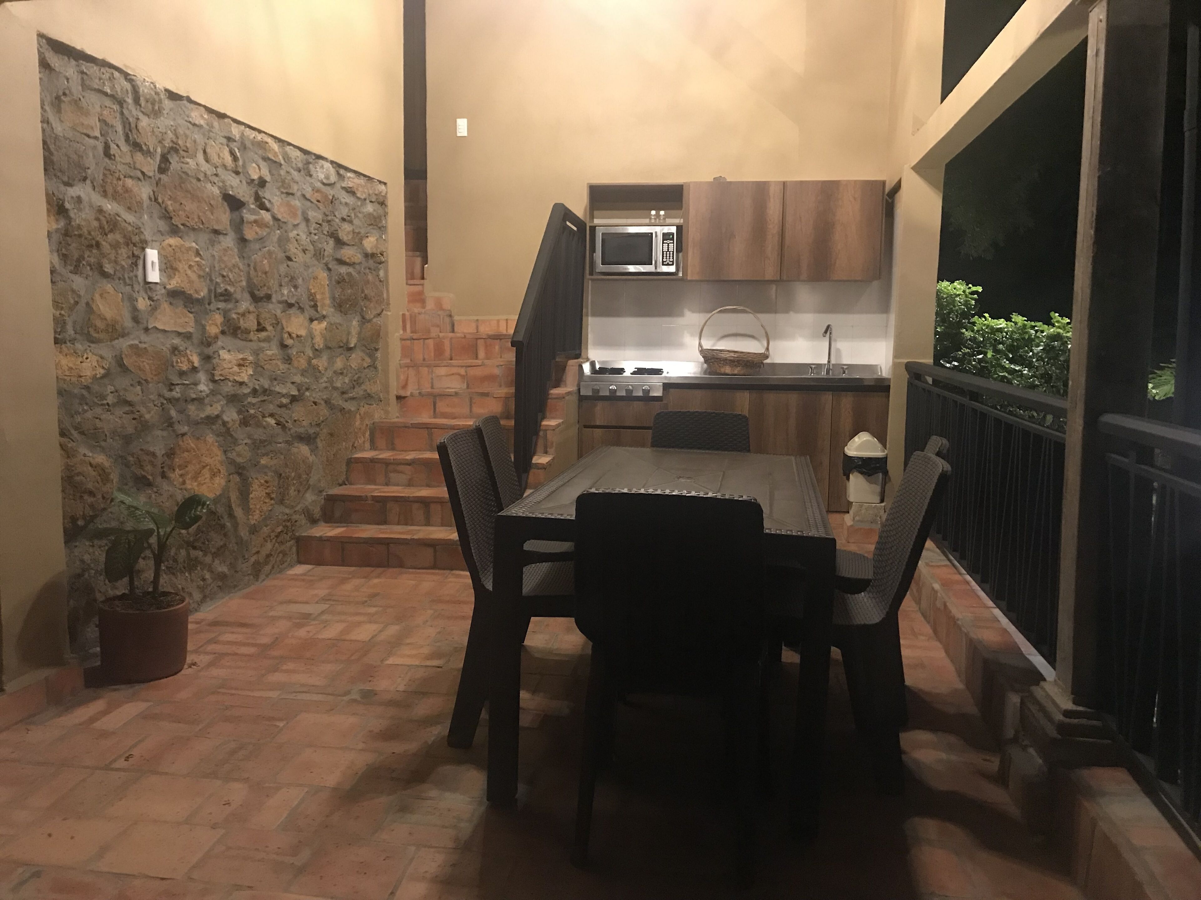 Un patio con una mesa y sillas, un muro de piedra, una zona de cocina con microondas y una pequeña planta en maceta.