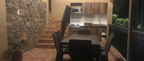 A patio with a dining table and chairs, a stone wall, a kitchen area with a microwave, and a small potted plant.