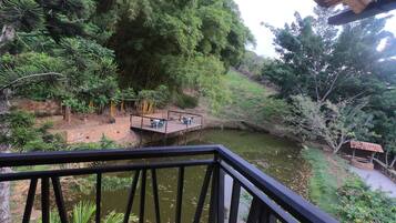 Une vue depuis un balcon donnant sur une rivière, avec une terrasse en bois et des chaises, le tout entouré d’une végétation luxuriante et d’arbres.