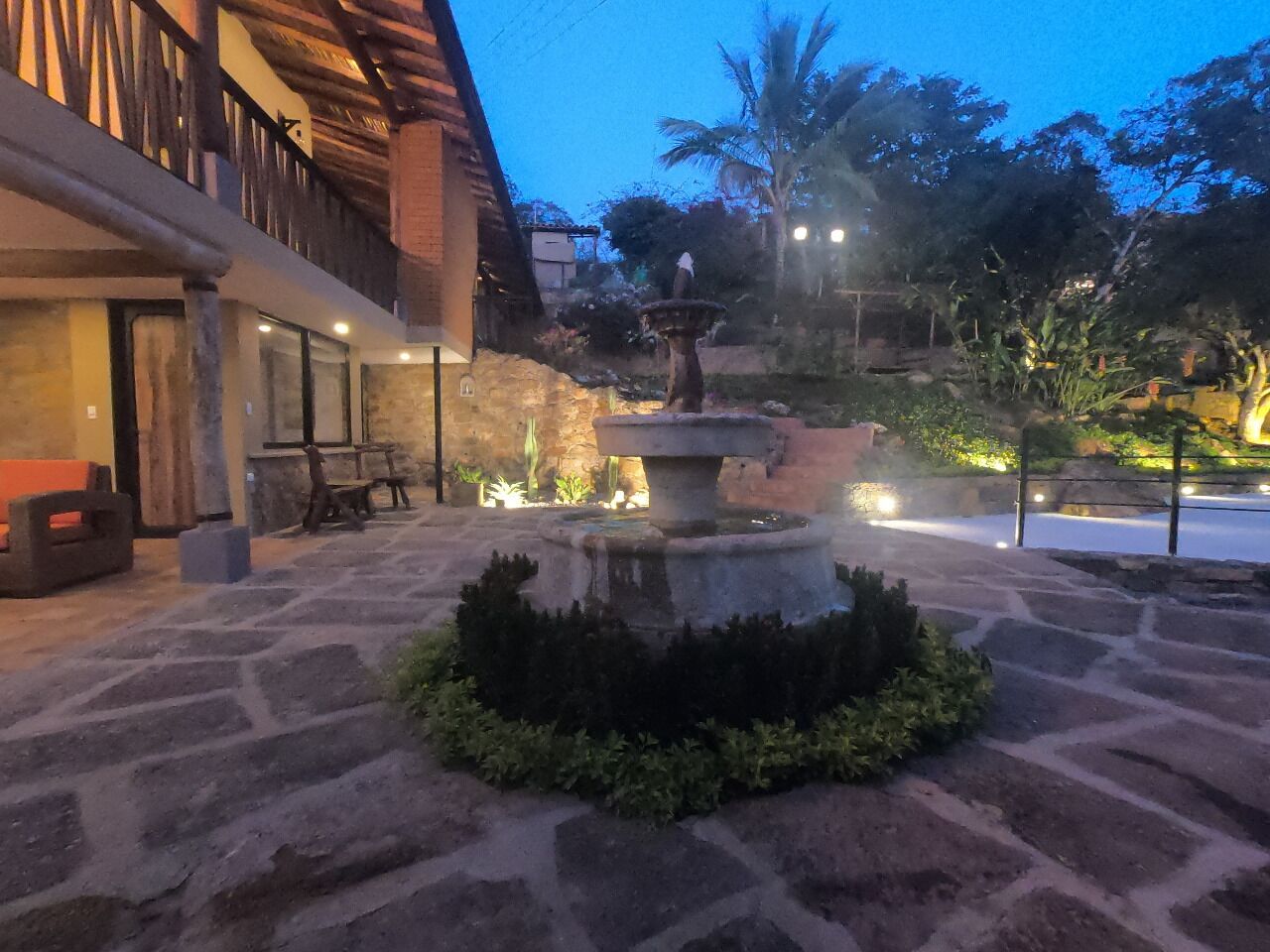 Un patio de piedra con una fuente central, asientos al aire libre y un edificio con un balcón de madera.