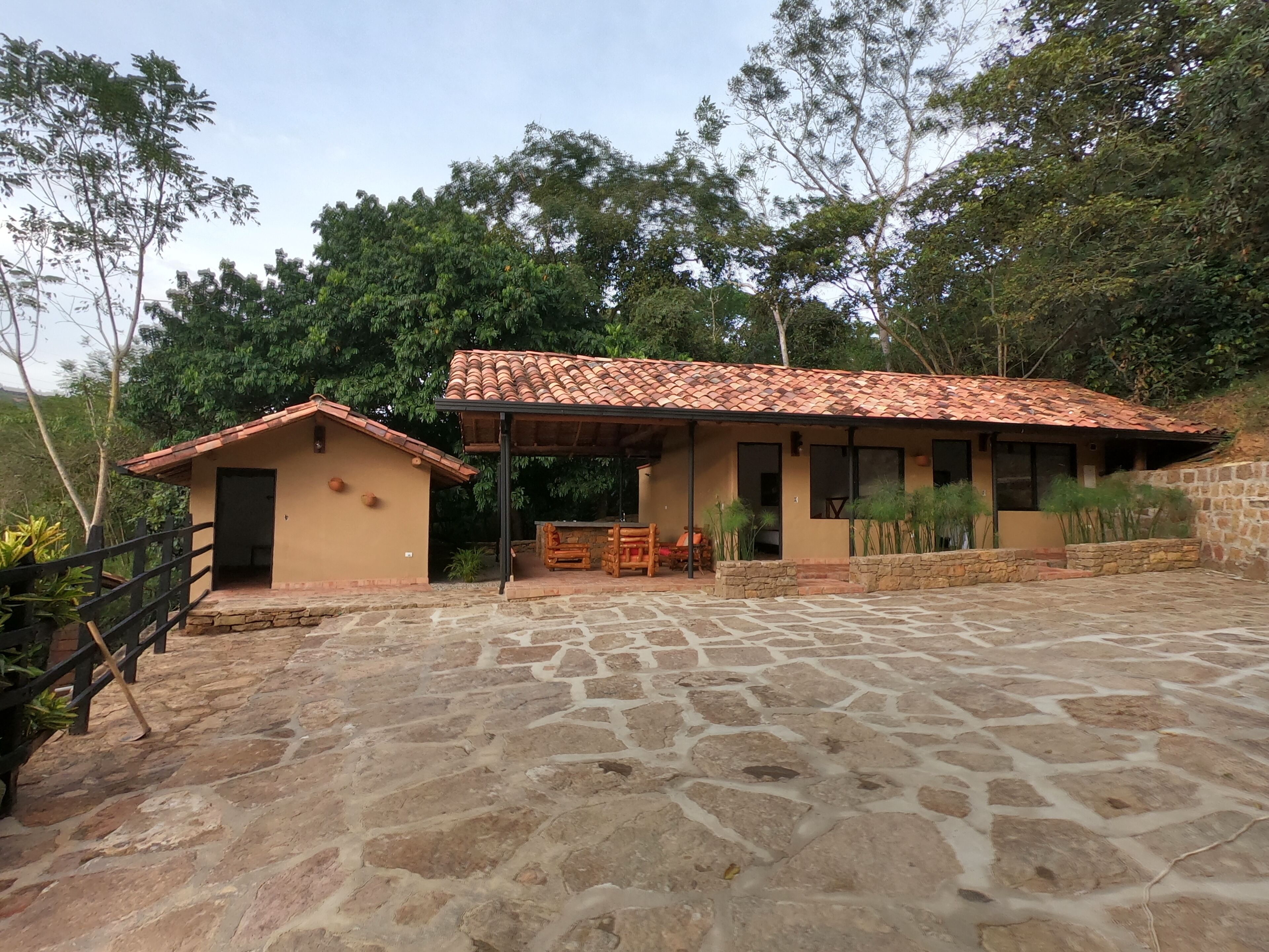 A rustic building with a tiled roof and stone flooring, surrounded by greenery.