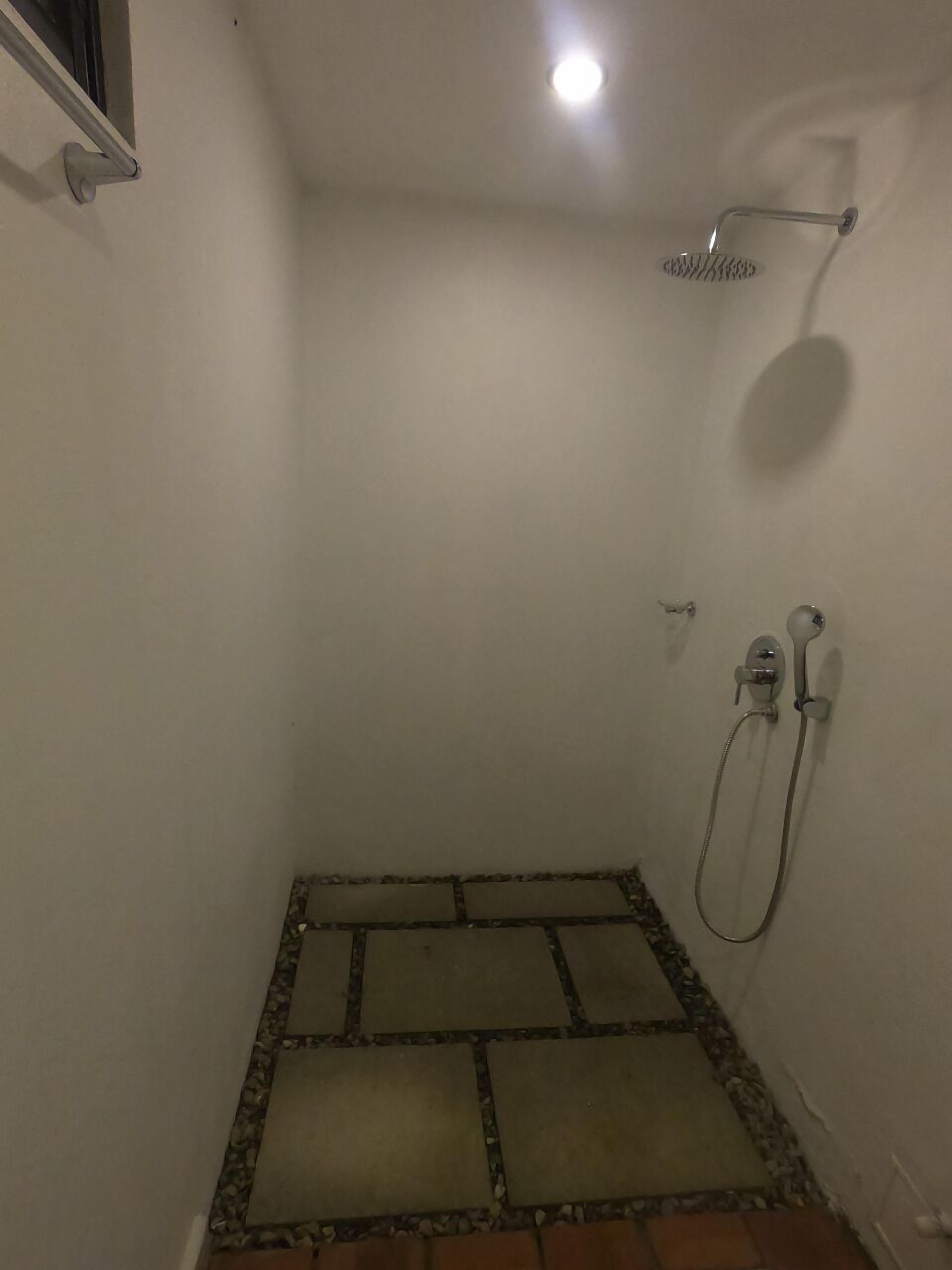 Un espace douche doté d’un sol carrelé, d’une douchette à main et d’un robinet mural.