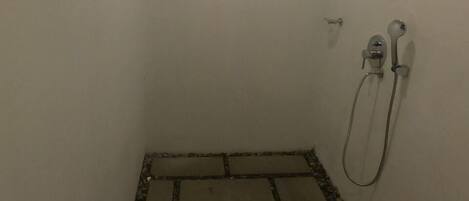 Un espace douche doté d’un sol carrelé, d’une douchette à main et d’un robinet mural.