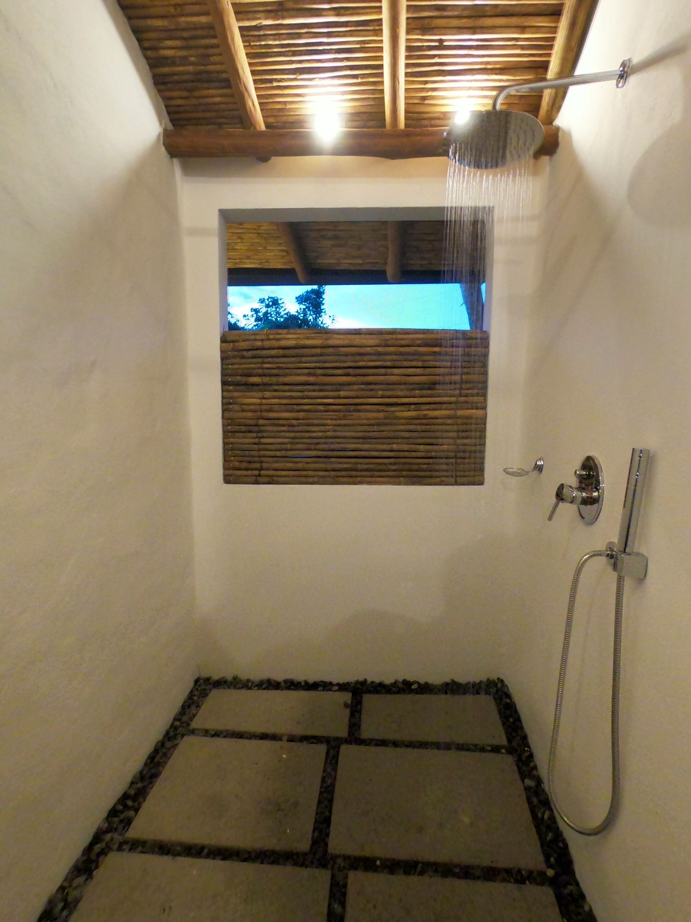 A shower area with a wooden ceiling, a window with blinds, and a tiled floor.