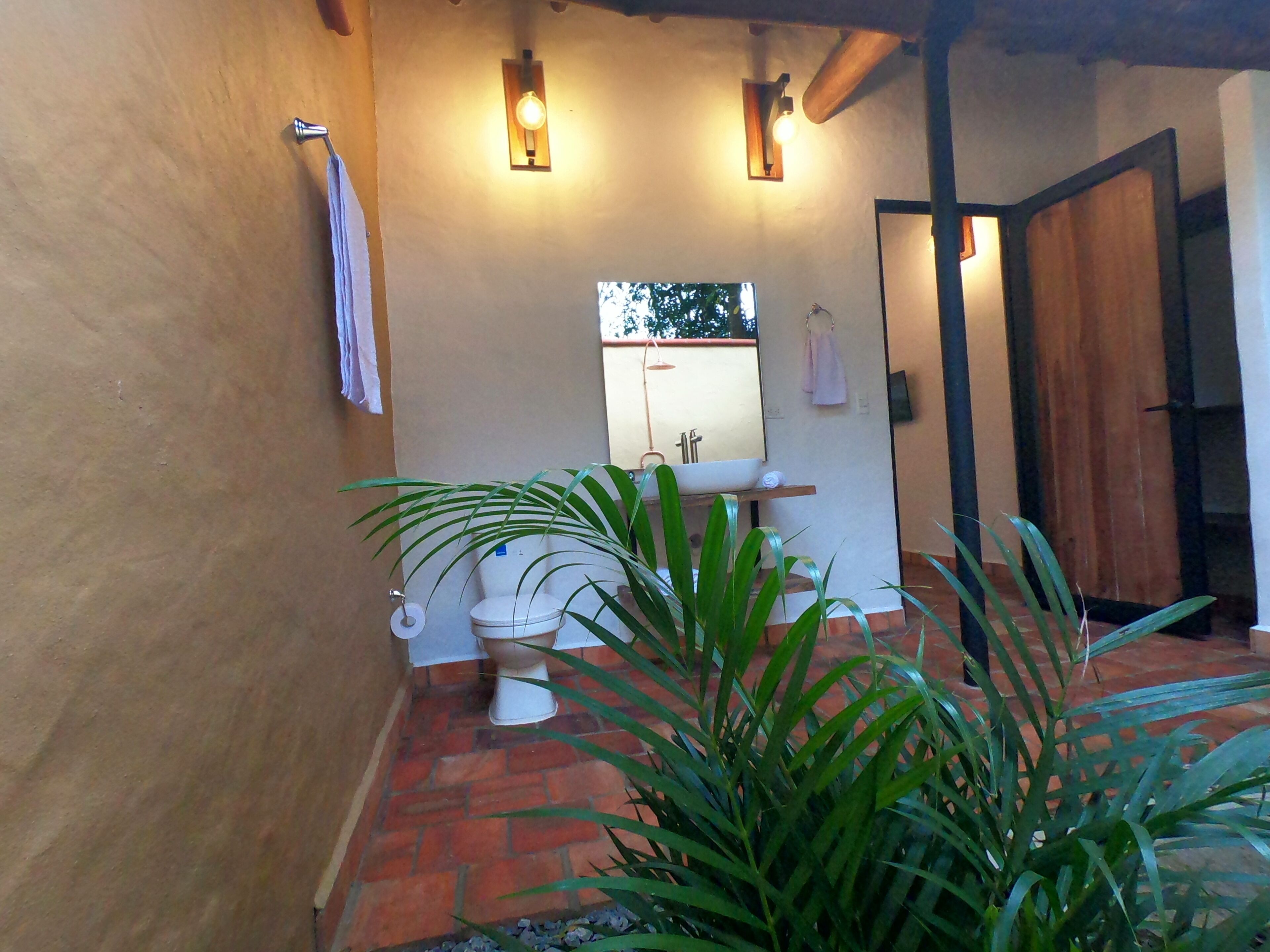 A bathroom with a toilet, sink, and shower area, featuring a brick floor and a wooden door.