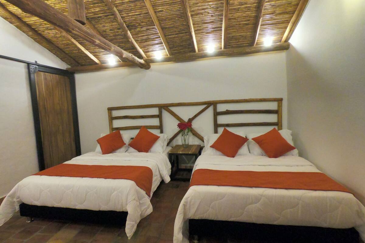 Ein Zimmer mit zwei Betten, jeweils mit weißer Bettwäsche und orangefarbenen Akzenten, Holz-Kopfteilen und einer rustikalen Decke.