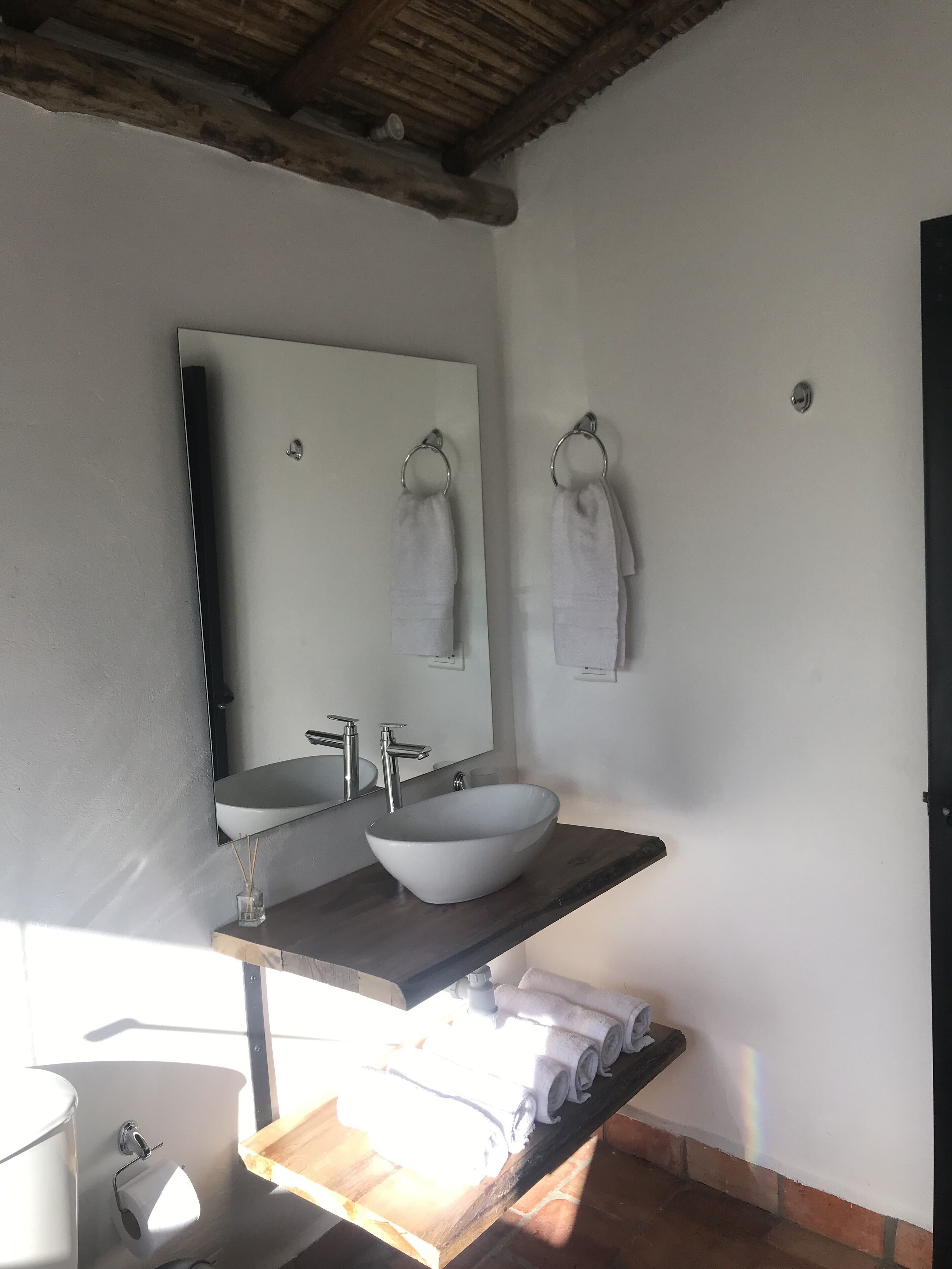 A bathroom with a large mirror, a white sink, and two towels hanging on hooks.