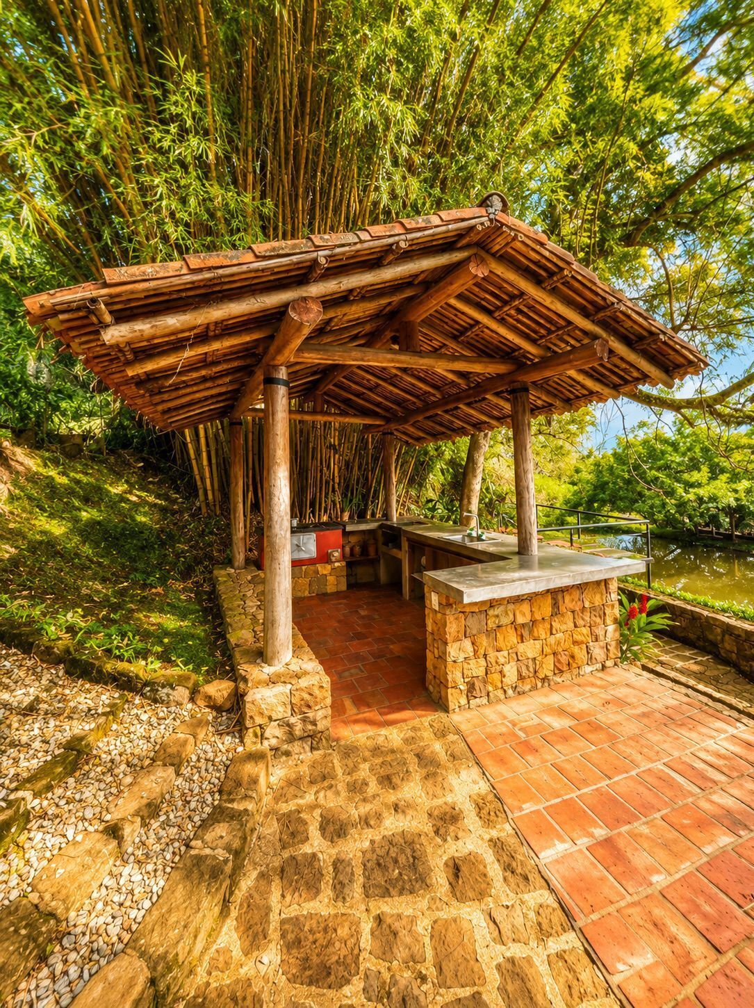 A bamboo structure with a stone base and a tiled floor, surrounded by greenery.