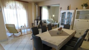 A dining area with a table and chairs, a sofa, and a cabinet in the background.