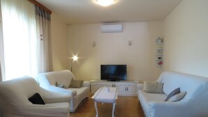 A living room with two white sofas, a coffee table, a flat-screen TV, and a white cabinet.