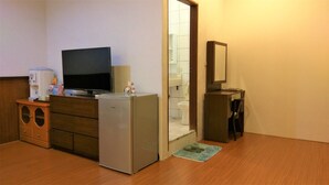 Une chambre d’hôtel compacte équipée d’une télévision, d’un minibar, d’un réfrigérateur et d’une petite salle de bain avec des toilettes et un lavabo.